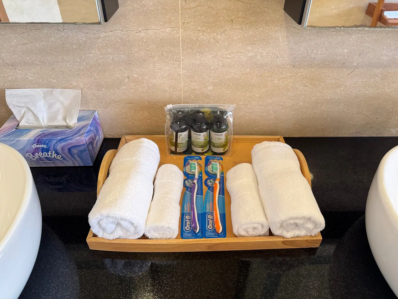 Rolled towels, toothbrushes and toiletries on a tray between the basins