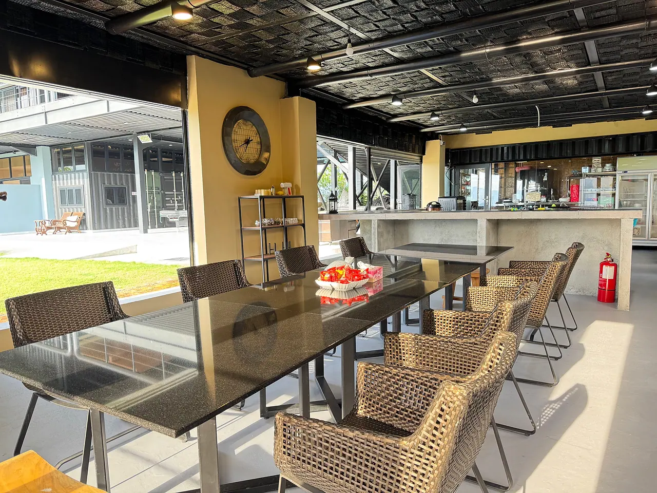 The indoor dining room: a long glass table with woven chairs, the kitchen counter behind