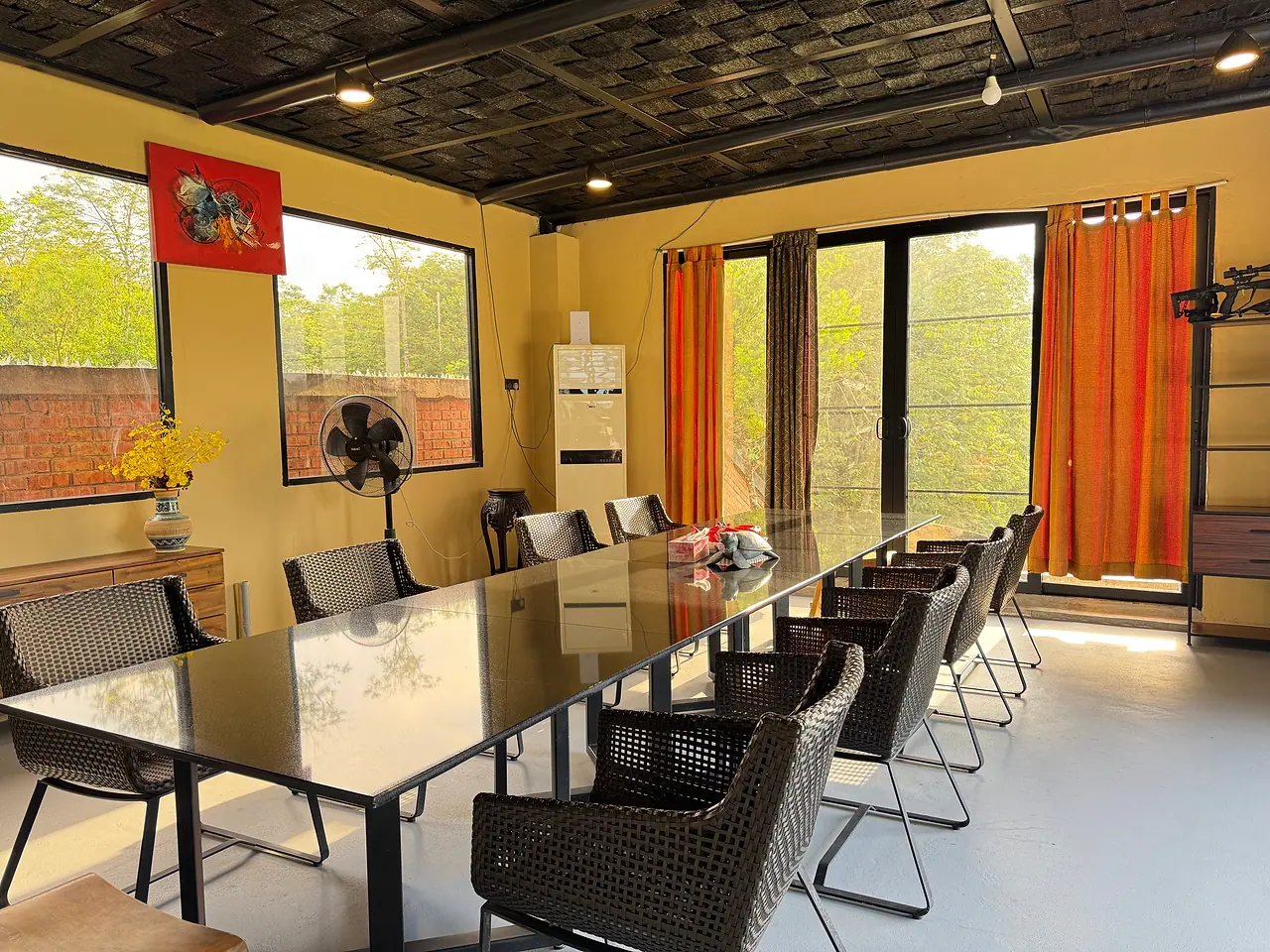 A second long dining table beside tall windows onto the trees