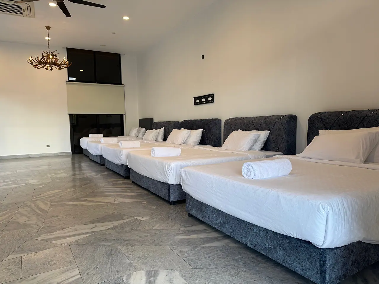 The family room: a row of queen and single beds on a marble floor, an antler chandelier above