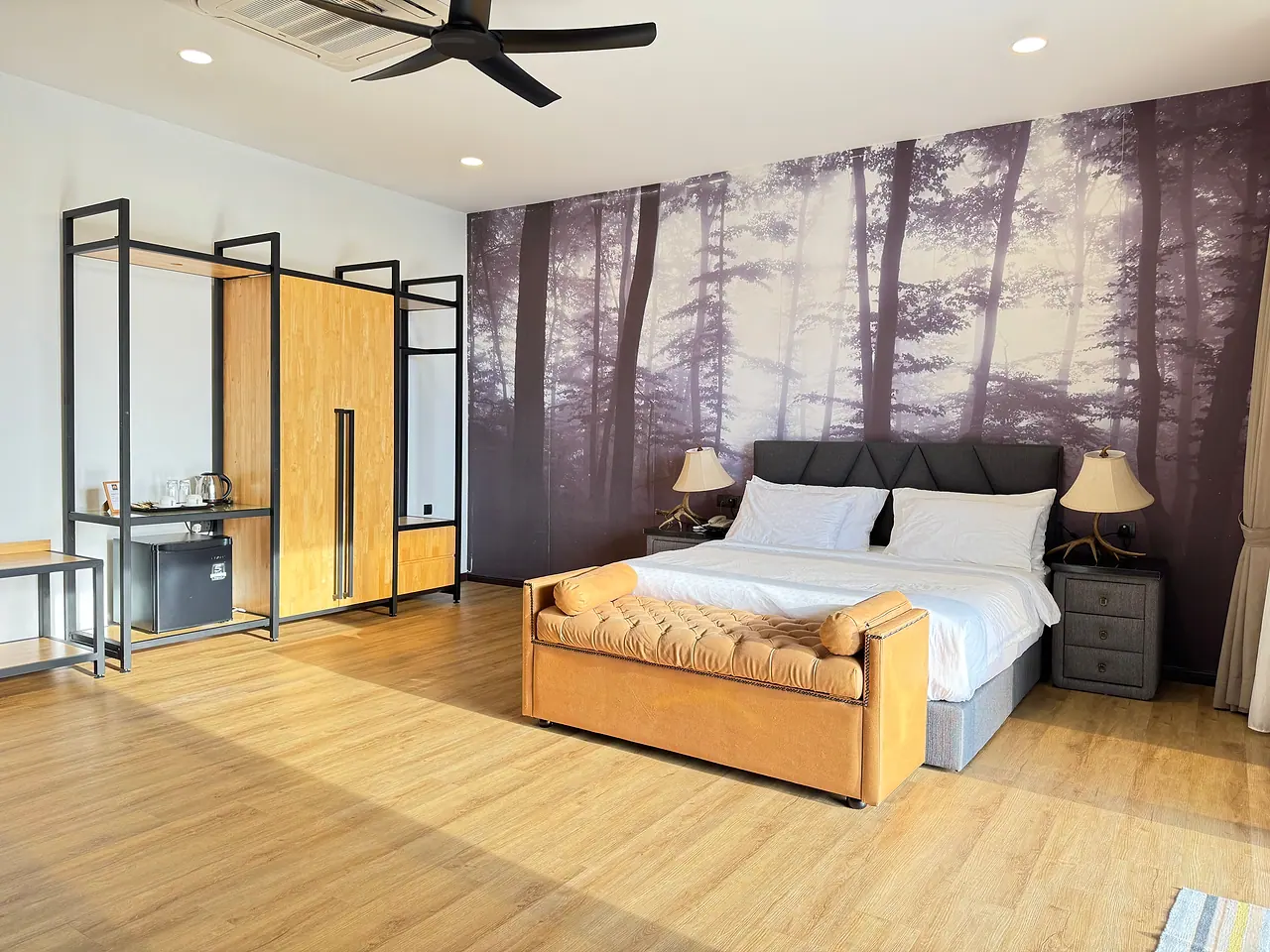 A deluxe king room: a king bed with a tan leather bench, a forest mural and an open wardrobe