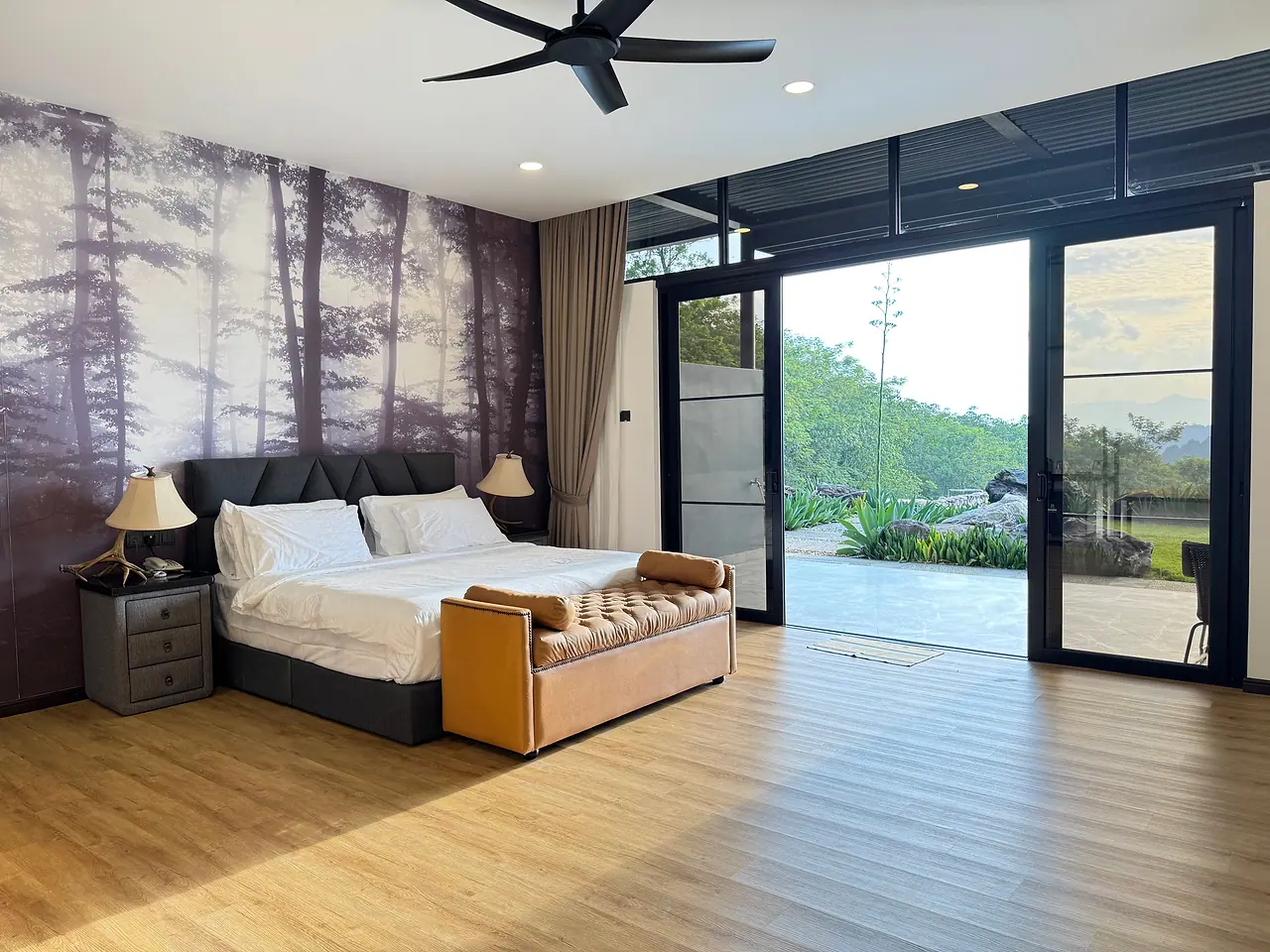 A deluxe king room with its glass doors open to the garden and the hills