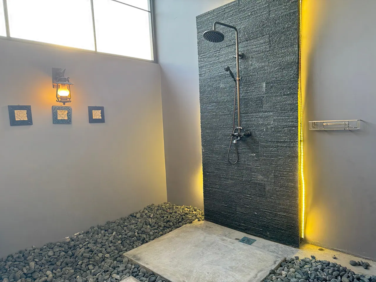 The outdoor shower of a deluxe room: a slate wall, a pebble floor and open sky