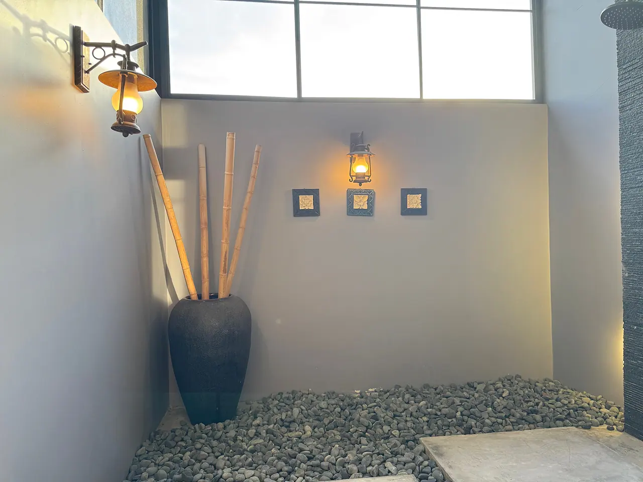 The outdoor shower courtyard, with a wall lantern and a tall vase of bamboo