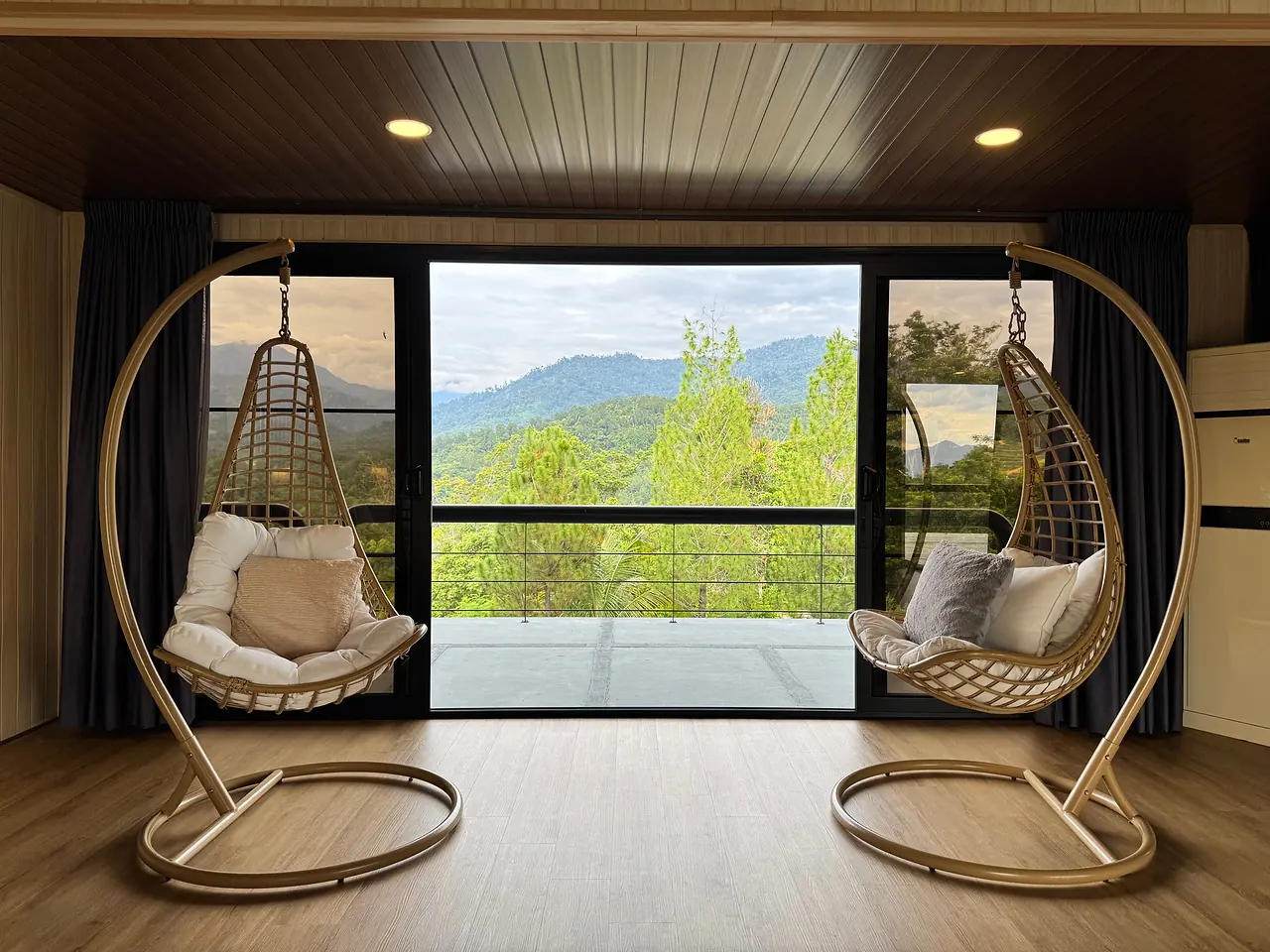 Two hanging rattan chairs at the penthouse window, facing forest and hills
