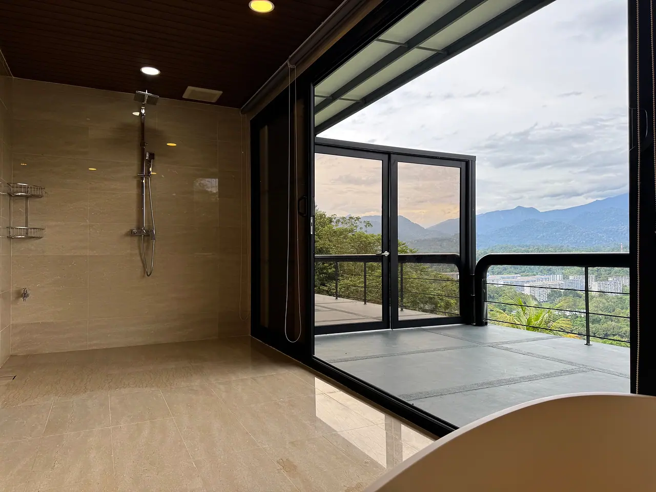 A walk-in shower in a penthouse bathroom, with glass doors onto the balcony and the hills
