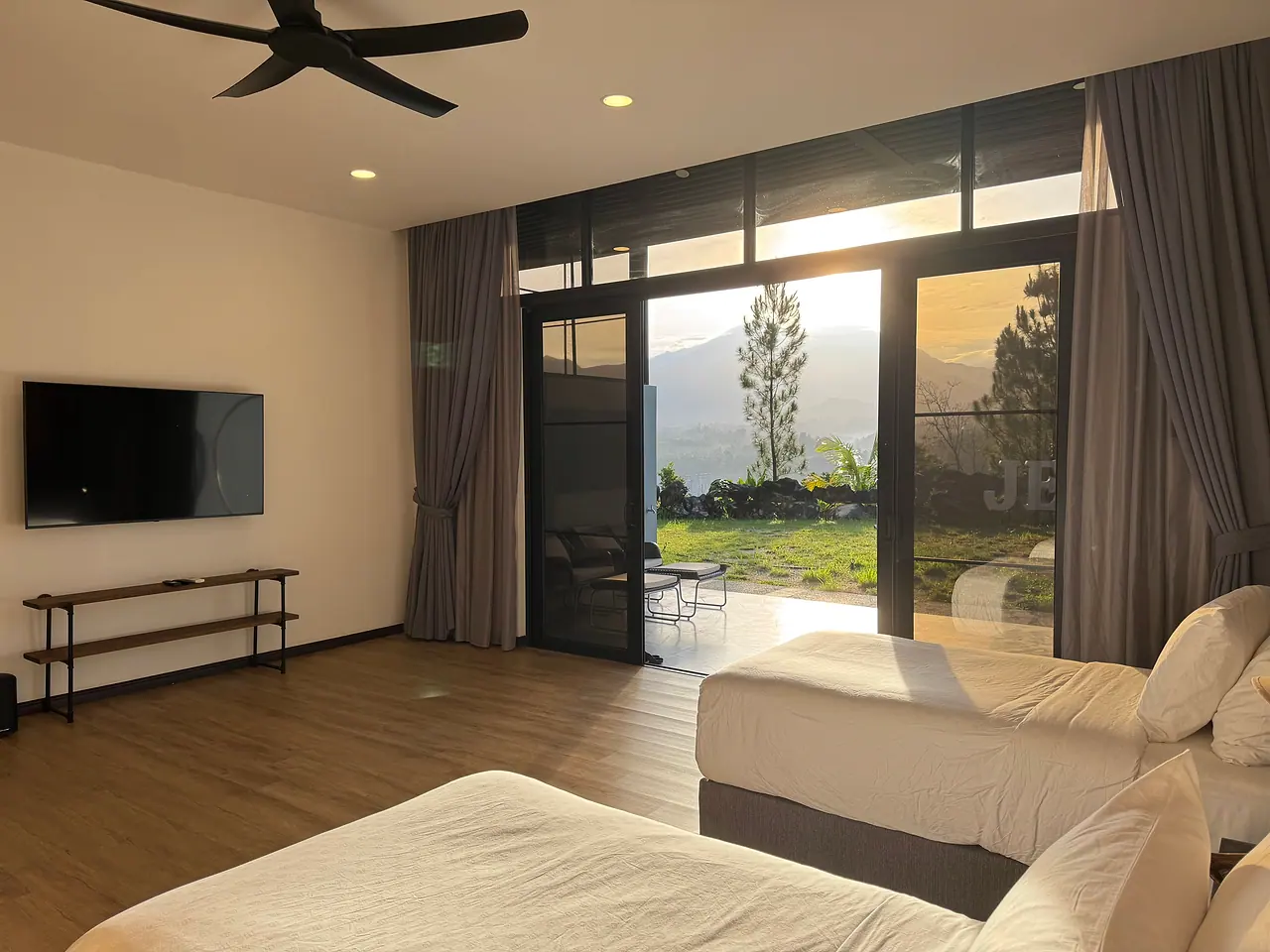 Two single beds and glass doors opening onto the lawn and hills in afternoon sun